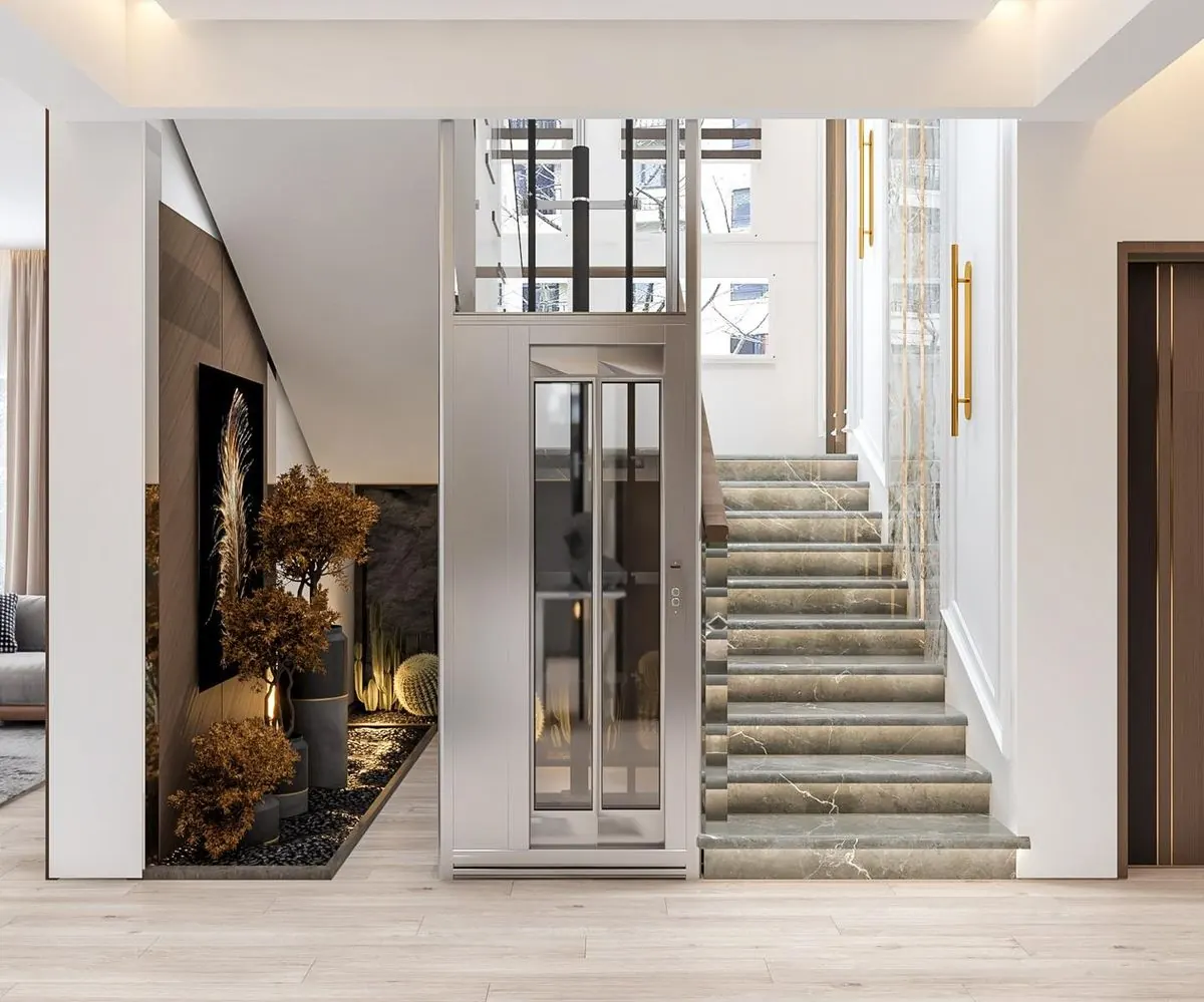 Compact silver-and-glass home lift beside a straight marble staircase in a bright villa interior