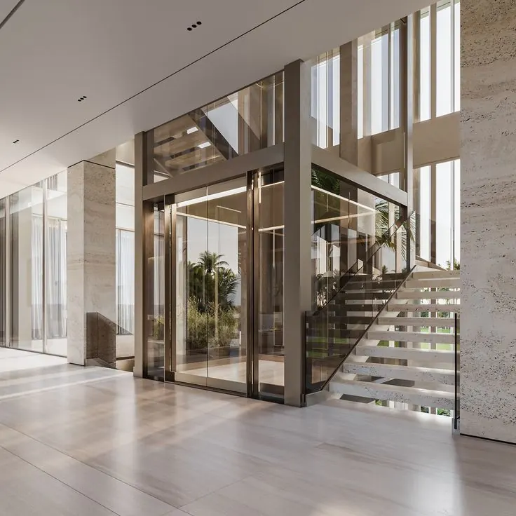 Bronze-framed glass home lift enclosure beside an open staircase in a bright villa interior